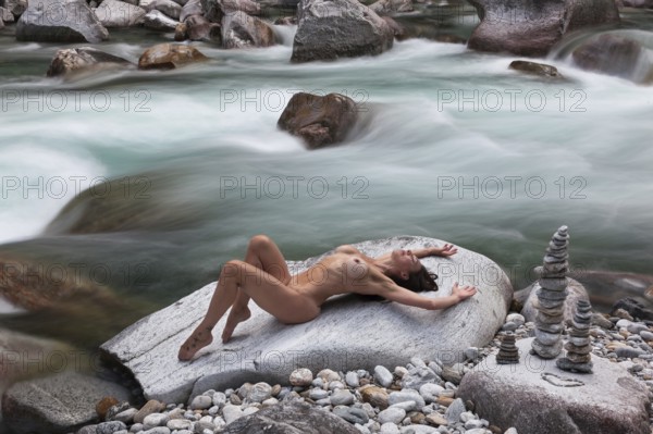 A woman in an elegantly professional pose on a rock, framed by flowing water, with pebbles stacked on top of each other to form cairns, aesthetic nude photography, outdoor shooting, Verzasca Valley, Valle Verzasca, Canton Ticino, Switzerland, Europe