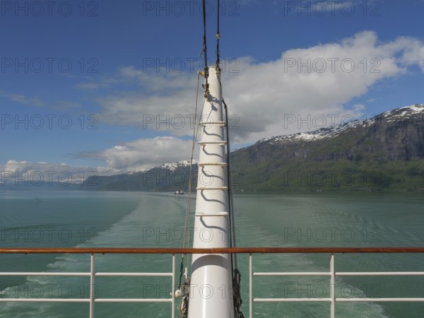 View from a boat access area over green water and surrounded by mountains and clouds, sailing in a fjord with green water and snow-capped mountains, Eidfjord, Norway, Europe