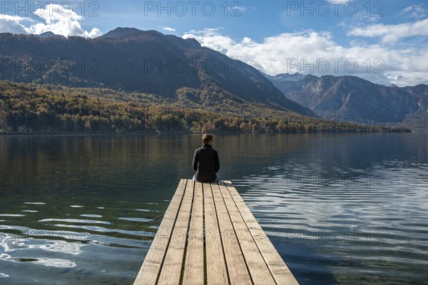 Sitting on a small jetty and enjoying the view on the landscape of lake Bohinj in the Triglav National Park, The Julian Alps, Slovenia, Europe