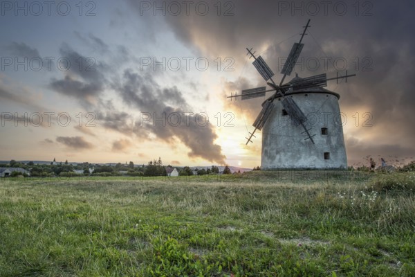 Windmill with wooden sails in a landscape with fields. Meadows and flowers appear in the sunset. Landscape shot in nature with a windmill. Historically atypical for the Balaton region in Hungary