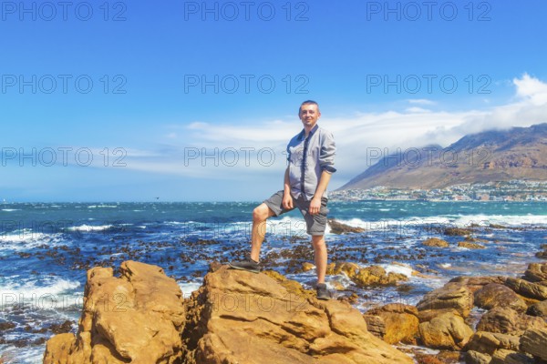 Male model tourist traveler at False Bay rough coast landscape with boulders waves and mountains with clouds in Glencairn Simons Town Cape Town Western Cape South Africa