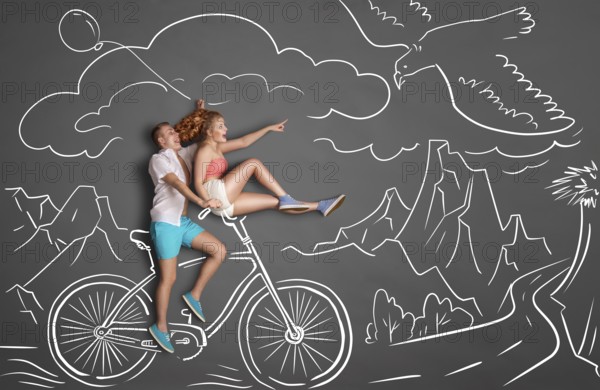 Happy Valentine's Day love story concept of a romantic couple on chalk drawings background of mountains. Male riding his girlfriend on a bicycle handlebar, female pointing at a flying eagle