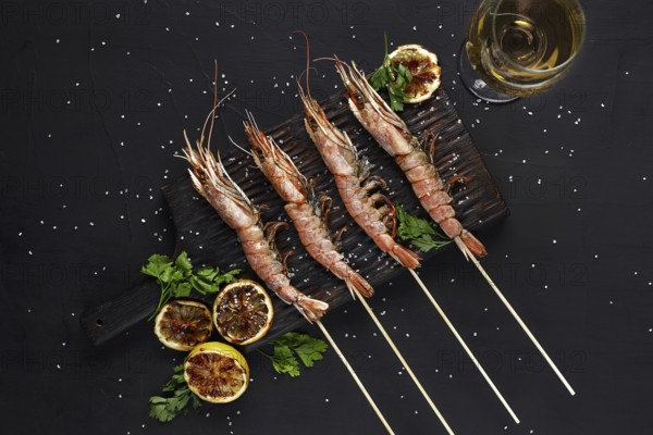 Grilled shrimp skewers. Seafood, shellfish. Shrimps Prawns skewers with herbs, garlic and lemon on black stone background, copy space. Barbecue shrimps prawns