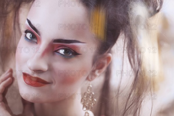Close up stylized portrait of a Japanese geisha with bright make up standing at the window watching the rain