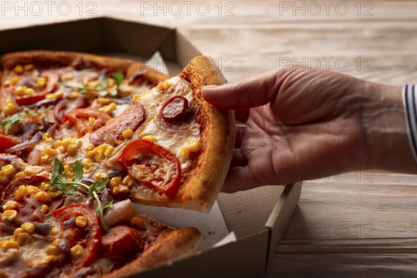 Human caucasian hand takes slice of large pizza from carton box on white wooden table