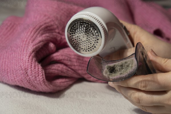Woman using Anti-pilling razor at home. Device for shaving clothes. Anti-Plush fabric Shaver. Electric portable sweater pill defuzzer Lint remover from pink acrylic or wool sweater. Slow fashion mending repairing clothes