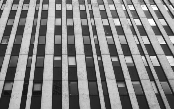 Close up perspective detail of tall high rise brutalist style office building with white vertical concrete lines and dark windows