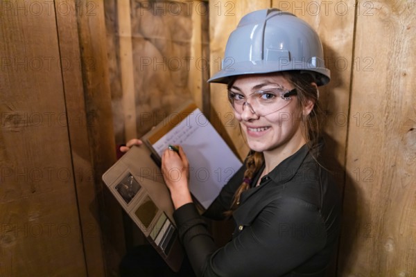 Indoor air quality inspector woman looking for molds or fungi problems on wooden walls and taking notes using her clipboard. she happy and smiling