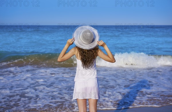 Girl with beach hat in sea open arms with summer white dress