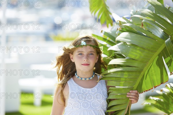 Blond kid girl at banana tree leaves in bright day light in Mediterranean