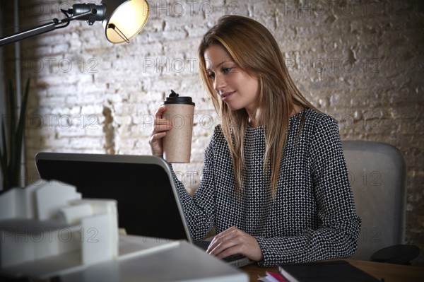 Businesswoman drinking coffee with laptop computer at office