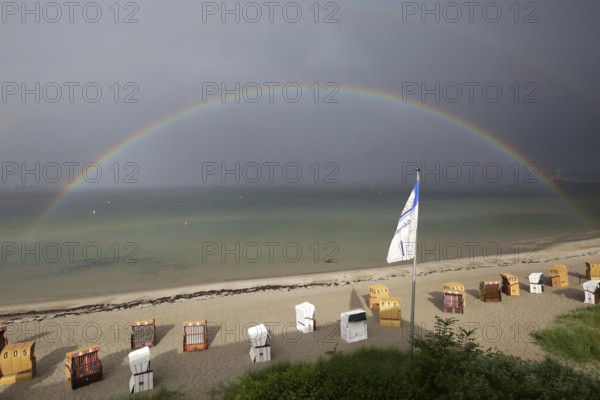 Rainbow over the sea, beach with beach chairs under a cloudy sky at the beach of Eckernförde