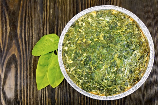Celtic cake with spinach, tomatoes, oatmeal and eggs in baking dish from a foil, spinach leaves on the background of wooden boards on top