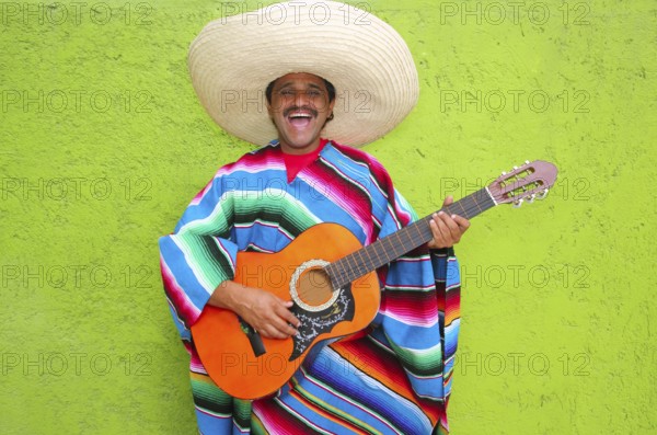 Mexican typical man playing guitar poncho on green wall