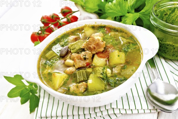 Soup with pisto sauce, pork fat, tomatoes, zucchini, beans, celery and leek in a bowl on a towel on light wooden board background