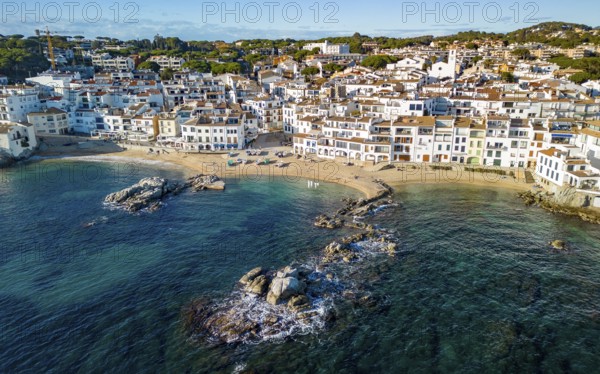 Aerial view of a picturesque coastal town with white buildings, sandy beach, and clear blue sea under a sunny sky, Calella de Plafrugell town, Costa Brava, Catalonia Spain