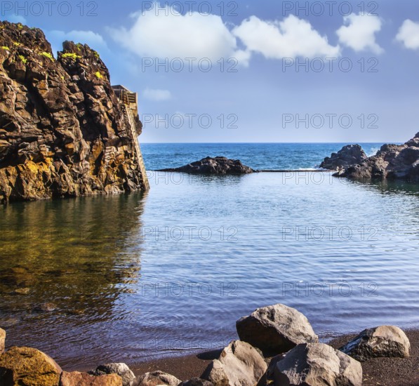 The stony shore of the Atlantic ocean. Small bay with smooth water. Volcanic island of Madeira. The concept of exotic and ecological tourism
