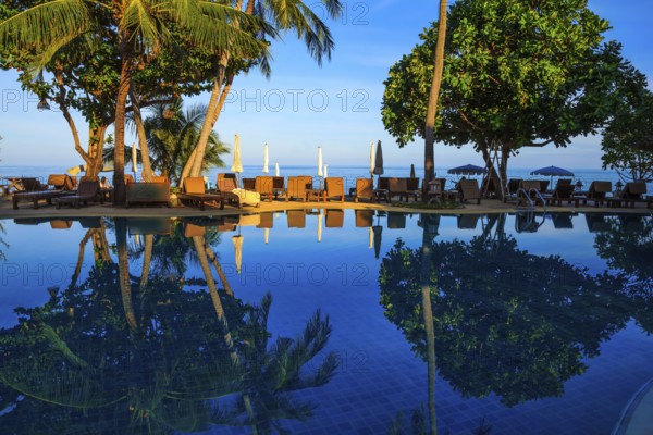 Sunset on the beach resort. An oceanfront pool surrounded by palm trees. Palm trees reflected in smooth water
