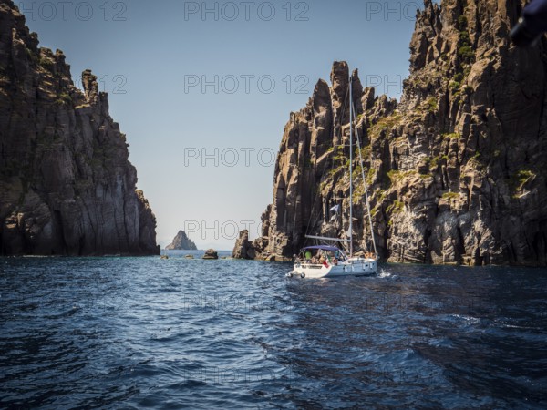 Modern white sailboat sailing slowly in rippling sea near rough rock in cloudless day on resort in Italy, Eolie islands