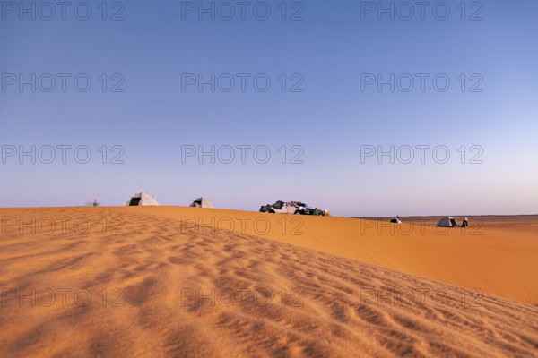 Tents and cars standing on a sand dune in the desert under a wide sky at sunset, camping in the sand dunes of the Sahara in Algeria
