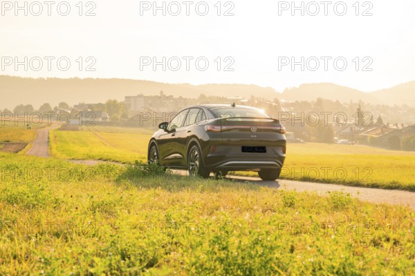 SUV driving on a country road with a view of a town at sunset, VW ID5 electric car, Calw, Black Forest, Germany