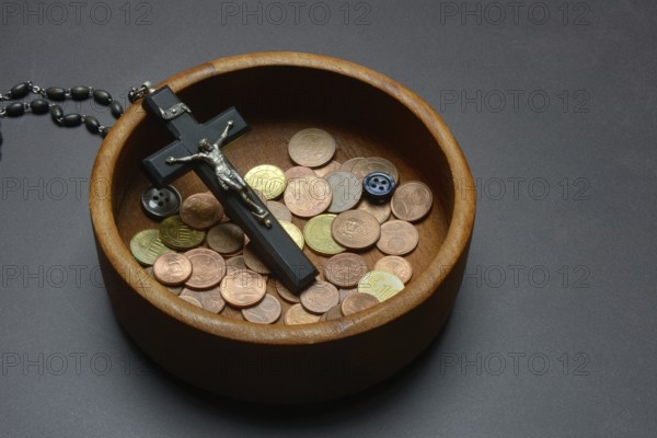 Crucifix with coins and buttons in a wooden bowl, church and money