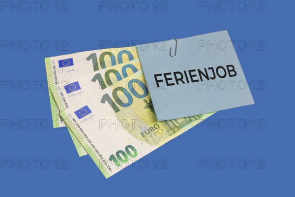 Holiday job symbol image: euro banknotes and a piece of paper with the words HOLIDAY JOB cut out against a blue background