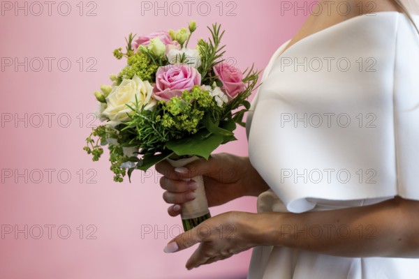 Bride holding bridal bouquet with roses in front of pink wall