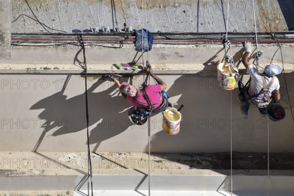 Painter hanging from a rope while working on a façade, symbolic image for safety in construction, Buenos Aires, Argentina