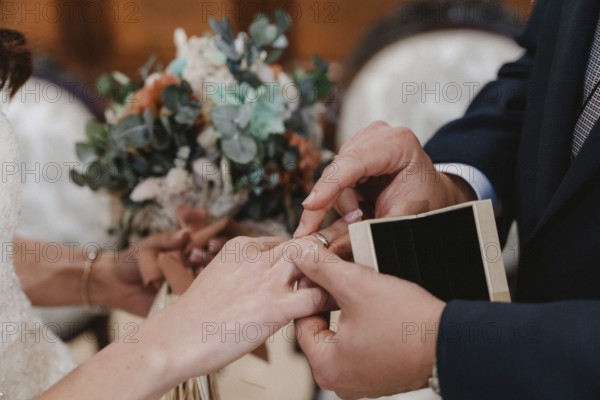 Close up of a couple exchanging rings during a wedding ceremony, with a beautiful bouquet in the background, symbolizing love and commitment
