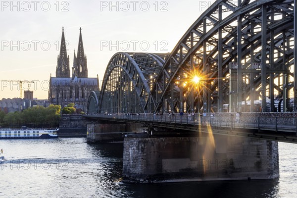 Cologne Cathedral in the evening with Hohenzollern Bridge, railway bridge over the Rhine. Sunset on the Rhine with sun star. City view of Cologne, North Rhine-Westphalia, Germany