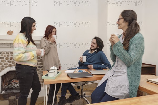 Four co-workers have coffee in the office, chat and have fun, taking a break