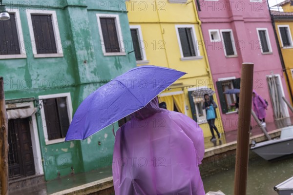 City view of Burano with colourfully painted houses and canals. Rainy weather, people are carrying umbrellas. Burano, Venice, Venezia, Italy