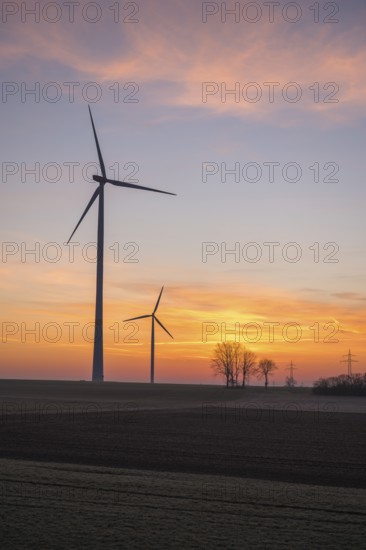 Three wind turbines in front of a beautiful sunset sky with trees, near Ulm, Swabian Alb, Baden-Württemberg, Germany