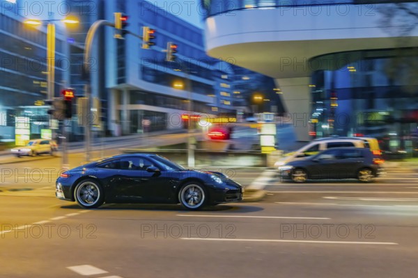 Porsche at night in front of urban surroundings with modern architecture, pull-along. Stuttgart, Baden-Württemberg, Germany