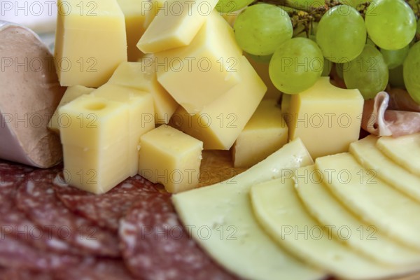 Cheese cubes and slices of sausage with grapes on a wooden board offer a classic savoury selection, Germany