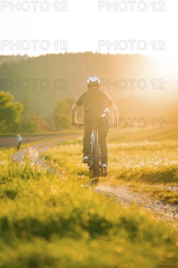 A person riding along a dirt track at sunset, surrounded by nature, e-bike, forest bike, Calw, district of Calw, Black Forest, Germany