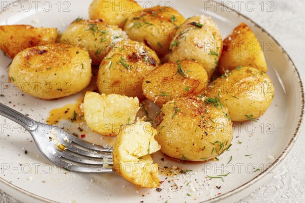 Half-eaten fried new potatoes, with butter and dill, on a white plate, with a fork, at home, no people