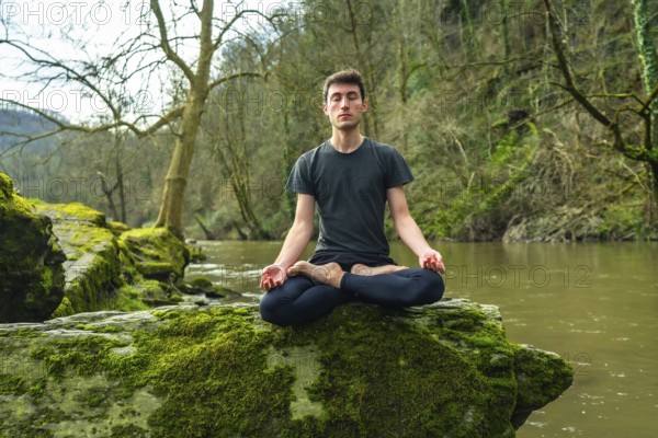 Yoga instructor meditating in lotus position on a mossy rock by a tranquil river, surrounded by lush nature, promoting mindfulness and serenity