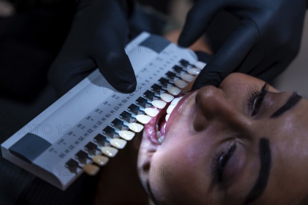 Dentist comparing patient's teeth shade with tooth whitening shade guide palette in dental clinic