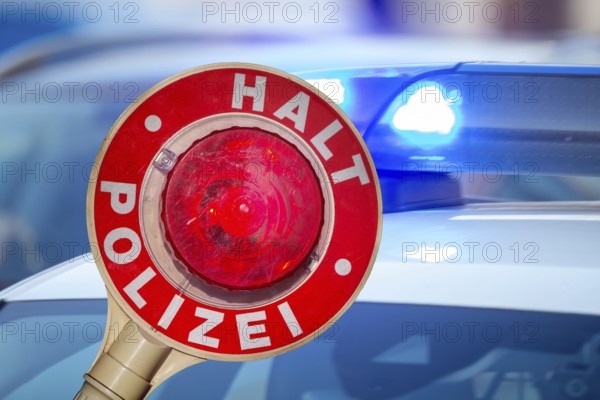 (Photomontage) Symbolic image of a police check: close-up of a police trowel labelled HALT POLIZEI in front of a police vehicle with flashing blue lights
