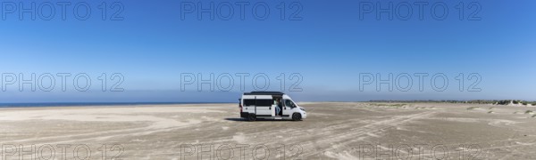 Ringby, Denmark: 31 May, 2021: panorama of a gray camper van parked on an endless white sand beach in the middle of nowhere with ocean behind