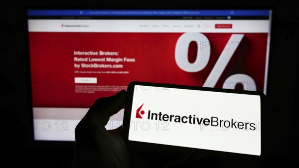 Stuttgart, Germany, 07-24-2022: Person holding mobile phone with logo of American company Interactive Brokers LLC (IB) on screen in front of web page. Focus on phone display