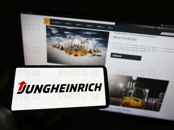 Stuttgart, Germany, 05-21-2022: Person holding smartphone with logo of German engineering company Jungheinrich AG on screen in front of website. Focus on phone display