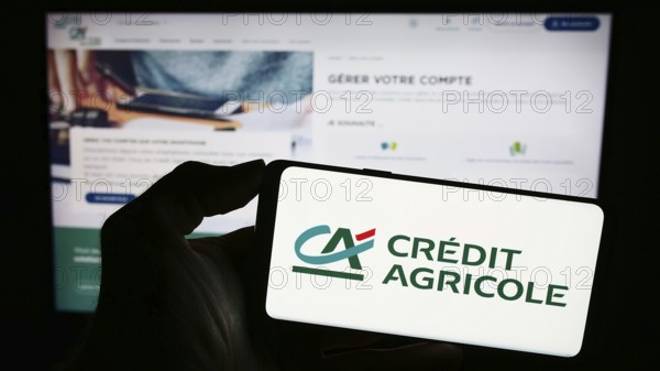 Stuttgart, Germany, 11-16-2023: Person holding smartphone with logo of French financial services company Crédit Agricole S.A. in front of website. Focus on phone display
