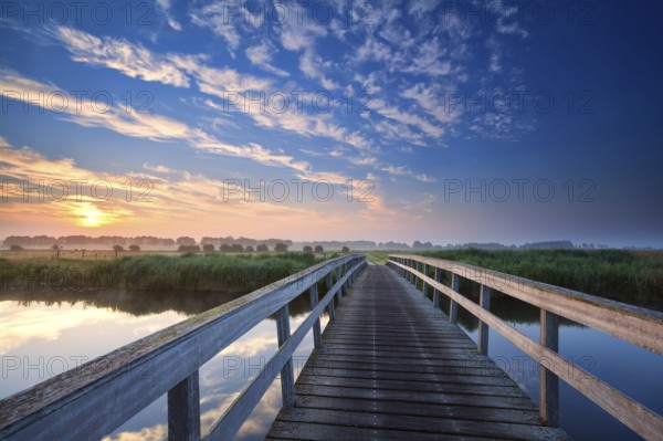 Wooden bridge over river at summer sunrise