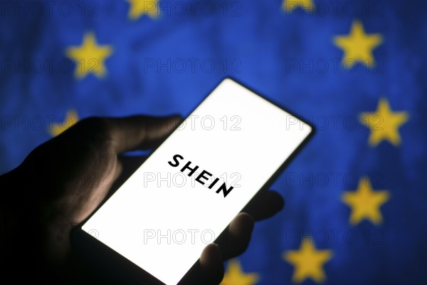 Smartphone with website of fashion e-commerce company Shein in front of business logo. Focus on top-left of phone display