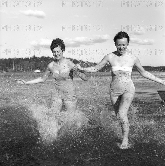 1950s summer. Two young women runs on the shallow part of the beach and the water splashes. Sweden 1959. Kristoffersson ref CG10-8