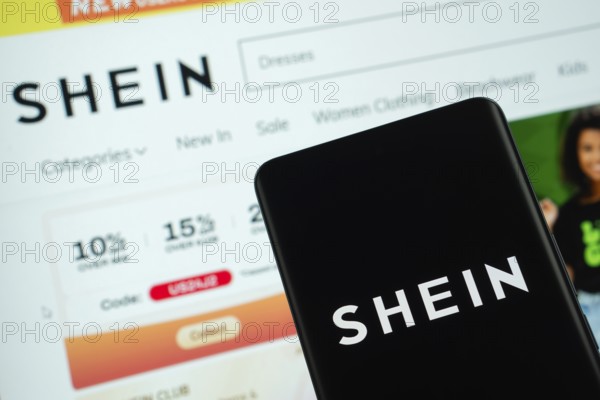 Dhaka, Bangladesh - 18 March 2025: The logo of the shein is displayed on a smartphone screen, and the website shein is visible on a computer screen in the background