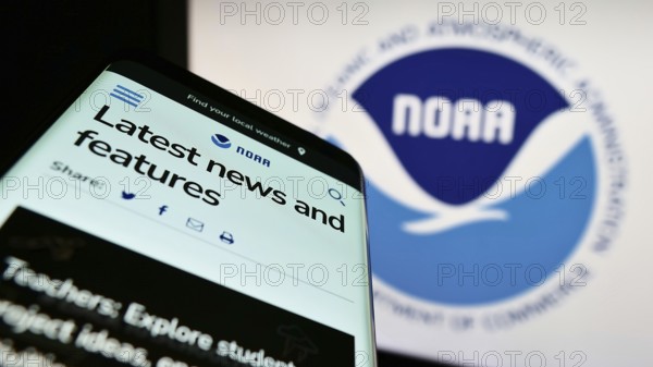 Stuttgart, Germany, 10-09-2022: Mobile phone with website of National Oceanic and Atmospheric Administration (NOAA) on screen in front of logo. Focus on top-left of phone display